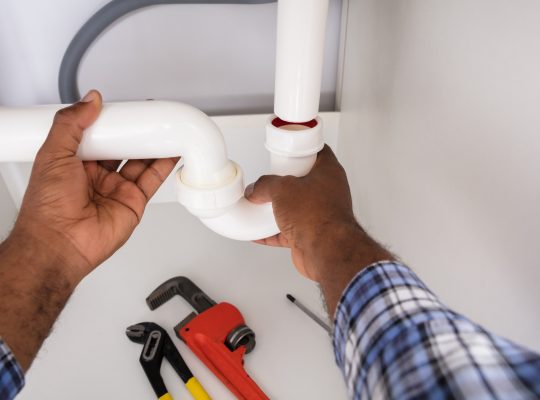 Close-up Of Plumber Fitting Sink Pipe In Kitchen At Home